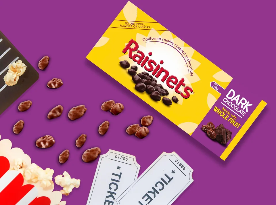 A Raisinets dark chocolate theater box with popcorn and movie tickets